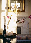 Flasche und brennende Kerzen auf Tisch mit weihnachtlich dekoriertem Kaminsims und Messing Kerzenständer vor Spiegel