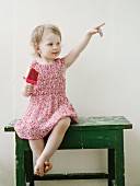 Little girl eating ice lolly sitting on small table