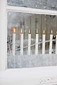 Row of lit candles behind frosty window