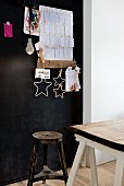 Vintage stool and old wooden table top on white trestles in front of black-painted pinboard with paper notes and stars