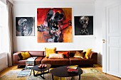 Lounge area with black metal coffee table in front of brown leather sofa below expressive paintings on wall