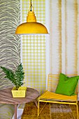 House plant on wooden table, yellow chair and yellow pendant lamp in front of strips of different wallpapers
