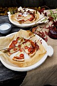 Small pizzas and baking parchment on rustic plates and arrangement of vine foliage on garden table