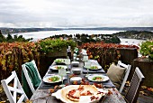 Herbstliche Stimmung über rustikal gedecktem Tisch mit Pizza und Salat; Blick auf norwegische Schärenküste im Hintergrund