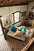 View from gallery down onto pale brick floor and bed with turquoise silk scatter cushions; paintings of Brazilian Candomble sea goddess on walls