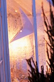 Blick auf Adventsstern durch erleuchtetes Fenster mit Eisblumen