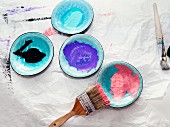 Paintbrushes and paint samples on ceramic saucers