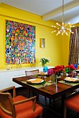 Solid wood dining table in yellow room with colourful, modern paintings and star-shaped pendant lamp