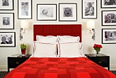 Red double bed framed by large collection of black and white photographs