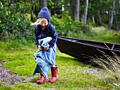 Child wearing hoody & towel on shore of lake with boat in background
