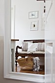 Wicker bag and rustic wooden bench with seat cushions reflected in mirror
