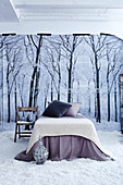 French bed with knitted blanket and scatter cushions on floor covered in artificial snow in front of poster of winter landscape