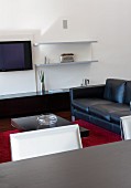 Modern living room with black sideboard and black leather couch; red woollen rug on floor