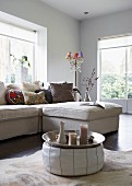 Bright living room with tray on pouffe as coffee table and comfortable couch; pretty standard lamp in corner