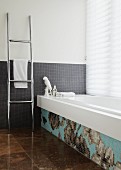 Bathroom with grey mosaic tiles on wall and bathtub decorated with floral mosaic