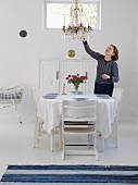 Woman in white dining room with set dining table & chandelier