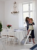Mother and daughter in dining room with set dining table & chandelier