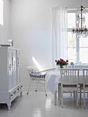 White interior with dining table, chandelier, cot & dresser