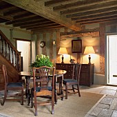 Antique furniture and foot of staircase in open foyer of rustic, half-timbered house
