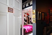 Blick in feminines Schlafzimmer mit weiß gestrichener Kassettentür und Bildergalerie im dunklen Flur