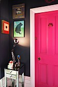 Glänzende Tischlampe beleuchtet kleine Bildersammlung an dunkelgrauer Wand neben pinkfarbener Kassettentür