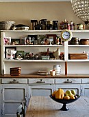 Ceramics, china crockery and framed photos on vintage-style dining room dresser; stemmed fruit bowl on simple wooden table in foreground