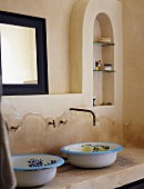 Rustikaler Waschtisch mit bemalten Emailschüsseln; darüber ein schwarz gerahmter Badezimmerspiegel neben Wandnische als kleines Badezimmerregal