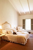 Cat on double bed with curved, Rococo-style headboard in simple attic bedroom with white wooden ceiling