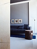 Elegant anthracite couch and rustic tree trunk side table on rich blue rug against grey wall