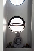 Statue of Buddha below open circular window in niche