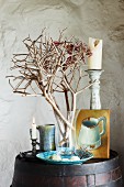 Beach finds in glass vase, two candlesticks and small oil painting on wooden barrel in corner of rustic room