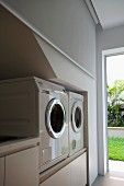 Utility room with elevated washer and dryer next to open door with view of sunny garden