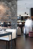 Moderner, mit grauem Marmor gefliester, offener Kamin als trennendes Element von Hotellounge und -restaurant