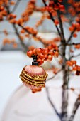 A vintage christmas bauble hanging from a branch of winter berries in a vase