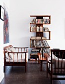 Unusual, winding bookshelves against white wall in simple, bright living room with delicate wooden furniture