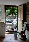 Kitchen with open wooden door and view of dog on terrace with table and bench against stone wall