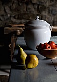 Pears next to bowl of tomatoes and white, vintage enamel pot with lid on wooden table