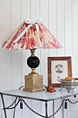 Table lamp with hand-crafted lampshade in red and white toile de jouy fabric on metal table against white, wood-clad wall