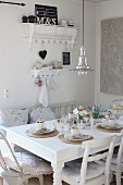 Retro lamp with metal lampshade above Easter table daintily set with white china on raffia place mats; romantic cushions on mismatched chairs and shabby chic ornaments on wall racks in background