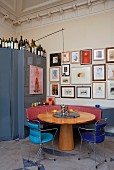 Round, Biedermeier-style wooden table and delicate metal chairs in front of collection of pictures on wall and blue metal cupboard with bottles on top