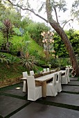Chairs with white loose covers around wooden table on terrace in tropical garden