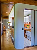 Kücheneinbau mit abgerundeter Ecke und offene Schiebetür mit Blick auf Küchenzeile, an der Seite Durchreiche und Thonet Barhocker