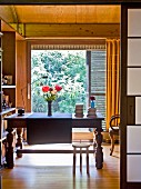 View though open sliding door of antique wooden table in front of floor-to-ceiling window in wood-panelled room with garden view