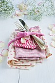 Stack of floral and striped fabrics and cutlery tied with a felt ribbon and scattered with petals