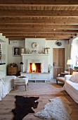 Sheepskin rugs between pale sofas and fire in open fireplace in comfortable, shabby-chic interior of Belgian holiday home