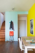 Office area in hallway of colourful apartment with coat pegs on wall and foot of wooden staircase