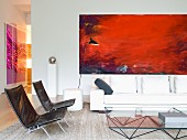 Easy chairs with metal frames and black covers in front of glass coffee table and white sofa below red modern artwork on wall