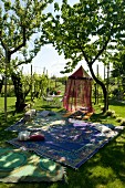 Sunny garden with patterned rugs on lawn and airy canopy hanging from tree