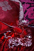 Still-life arrangement of champagne saucers next to bead necklace on red velvet cloth