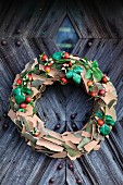 Decorative wreath made from pieces of bark and rosehips hanging on rustic wooden door